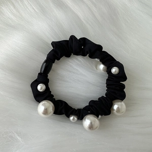 Detailed macro view of black elastic hair tie with elegant white pearls on plush background