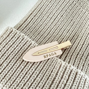 Detailed macro view of the pink and gold acetate hair clip with brand logo on knit background