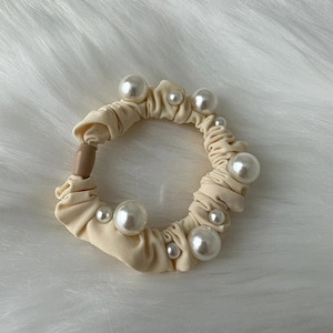 Close-up of cream elegant scrunchie with white pearls on soft plush background