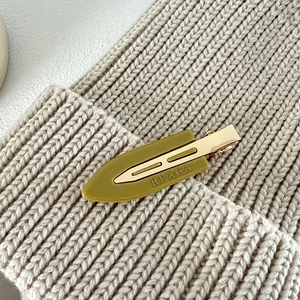 Detail of olive green acetate hair clip with gold metal clasp and RPAGA logo text