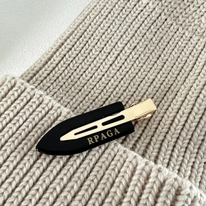 Detailed close-up of a black spindle hair clip with a gold metal base and logo lettering