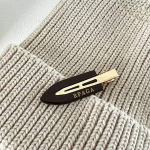 Detail of dark tortoiseshell acetate hair clip with golden metal accents on knit