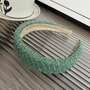 Green knit headband with shiny threads detail on a textured glass surface