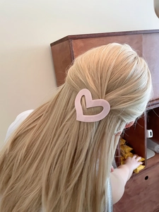 Pink heart hair claw clip made of acetate worn by a blonde model in a cozy home setting