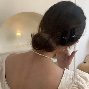 Elegant black velvet bow hair clip with pearls shown on a woman in a french style setting