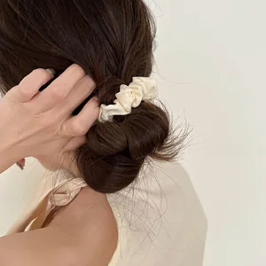 Detail of a creamy white silk scrunchie styled in a low bun with a soft satin finish