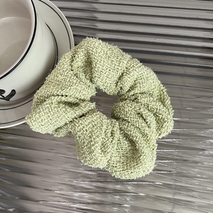 Detailed texture of light green tweed fabric on a stylish hair scrunchie accessory