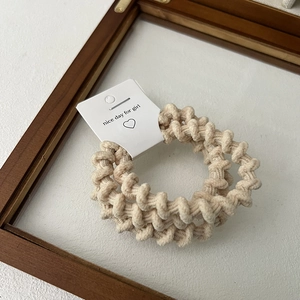 Detail of two beige spiral hair ties with fabric texture on white display card