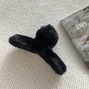Détail d'une pince à cheveux élégante en peluche noire sur fond tricoté beige