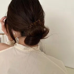Detail of dark brown satin scrunchie on hair bun in a cozy home setting back view