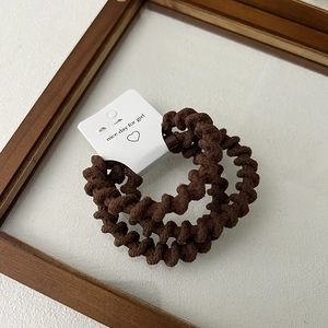 Close-up of two coffee brown spiral telephone wire hair ties on a white display card