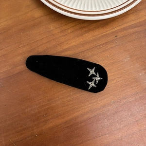 Detail of a black velvet teardrop hair clip with silver rhinestone star accents