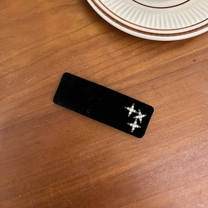 Detail view of a black velvet hair clip with silver rhinestone star patterns on wood