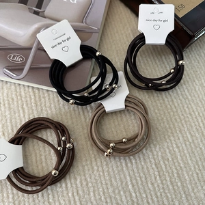 Close-up of elastic hair bands with gold beads on display card against beige fabric