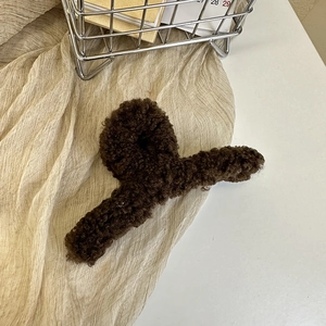 Close-up of soft brown faux fur hair claw clip resting on cream textured fabric