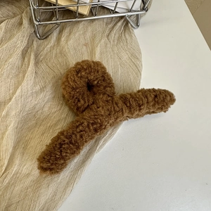 Close-up of brown plush faux fur hair claw clip on soft textured fabric background