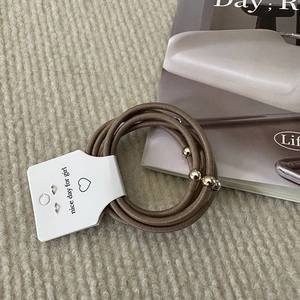 Close-up of elastic brown hair bands with gold metal beads on display card