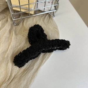 Detailed view of black plush faux fur hair claw clip resting in a metal basket