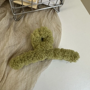 Detail of soft avocado green faux shearling plush hair claw clip on textile background