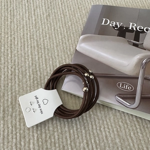 Close-up of dark brown braided hair ties with silver metal beads on a display card
