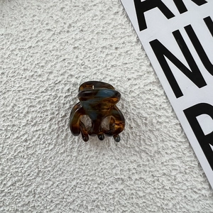 Detail view of mini acetate hair claw with tortoiseshell pattern on white textured background