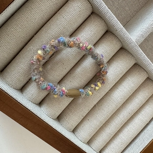 Detail of colorful plush scrunchie with multi-color knit texture in a wooden tray