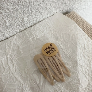 Close-up of minimalist beige snap hair clips in elegant packaging with handmade label