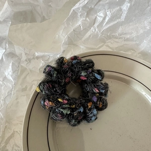 Détail d'un chouchou en peluche gris foncé avec des petits pompons colorés et texturés