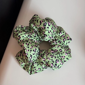 Détail d'un chouchou en satin à imprimé léopard vert fruit avec des taches roses
