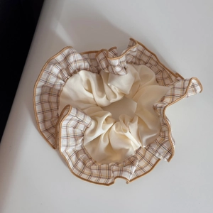 Macro detail of plaid fabric hair scrunchie with ivory stitching and ruffled texture