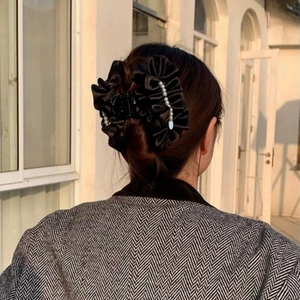 Detail of large black satin hair claw clip with bow design and white pearls for women
