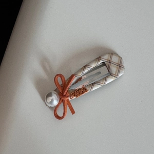 Detail of checkered fabric hair clip with a cute orange bow and white pearl accent