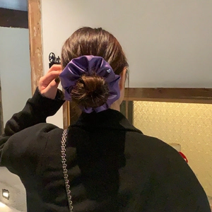 Elegant purple satin scrunchie styled on a woman's brown hair bun in a warm indoor setting
