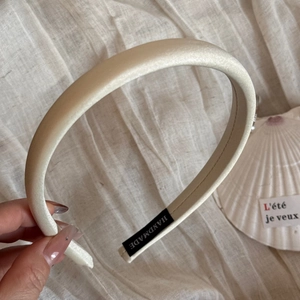 Détail d'un serre-tête en satin blanc crème avec étiquette faite main sur fond en lin