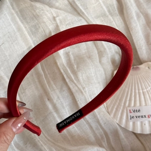 Détail d'un serre-tête en satin rouge fait main montrant l'étiquette sur tissu en coton beige