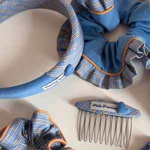 Detailed shot of blue checkered fabric hair accessories with orange piping and woven label