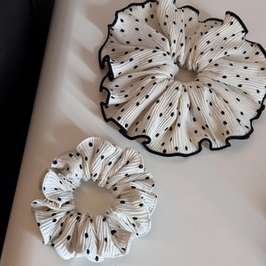 Close-up of pleated white fabric scrunchies with black polka dots in two sizes
