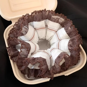 Détail d'un chouchou à rayures brunes avec dentelle café dans une boîte cadeau