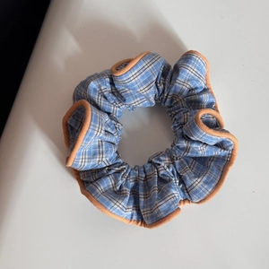 Detailed view of blue plaid fabric scrunchie with orange piping and elastic texture