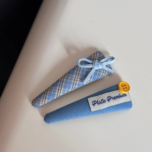 Detailed macro view of two blue fabric hair clips with a plaid pattern and yellow button
