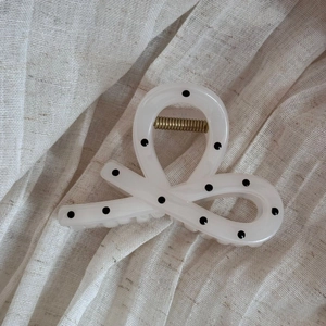 Detailed view of beige polka dot hair claw clip with elegant curved cross design