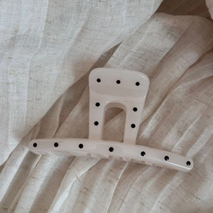 Detailed close-up of cream white hair claw clip with black polka dots on linen texture