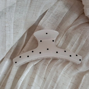 Detail of cream hair claw clip with black polka dots on beige linen background