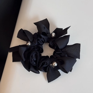Détail d'un chouchou en satin noir avec perles grises et élégants rubans à nœuds