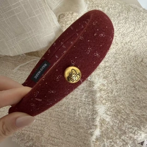 Macro detail of wine red fabric hair clip with golden butterfly button and handmade label