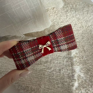 Detailed shot of red plaid ribbon hair clip featuring a gold metal bow ornament texture