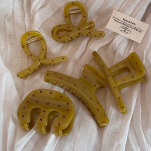 Close-up of olive green hair clips with red polka dots on white linen fabric