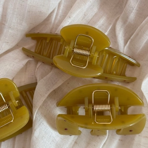 Detailed macro view of olive green resin hair clips with red polka dots and gold springs