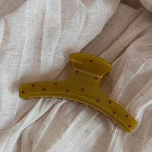 Detail view of olive green hair claw clip with red polka dots on white fabric background