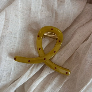 Detail of olive green resin hair claw clip with red polka dots on white soft fabric